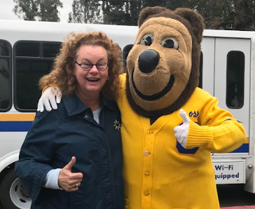 Image of a smiling woman with her arm around Oski the Bear. Both are giving a thumbs up.